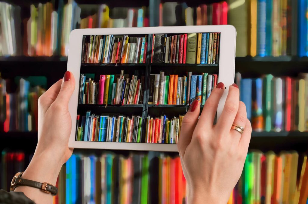 zwei Frauenhände fotografieren Bücher in einem Regal mit einem Tablet